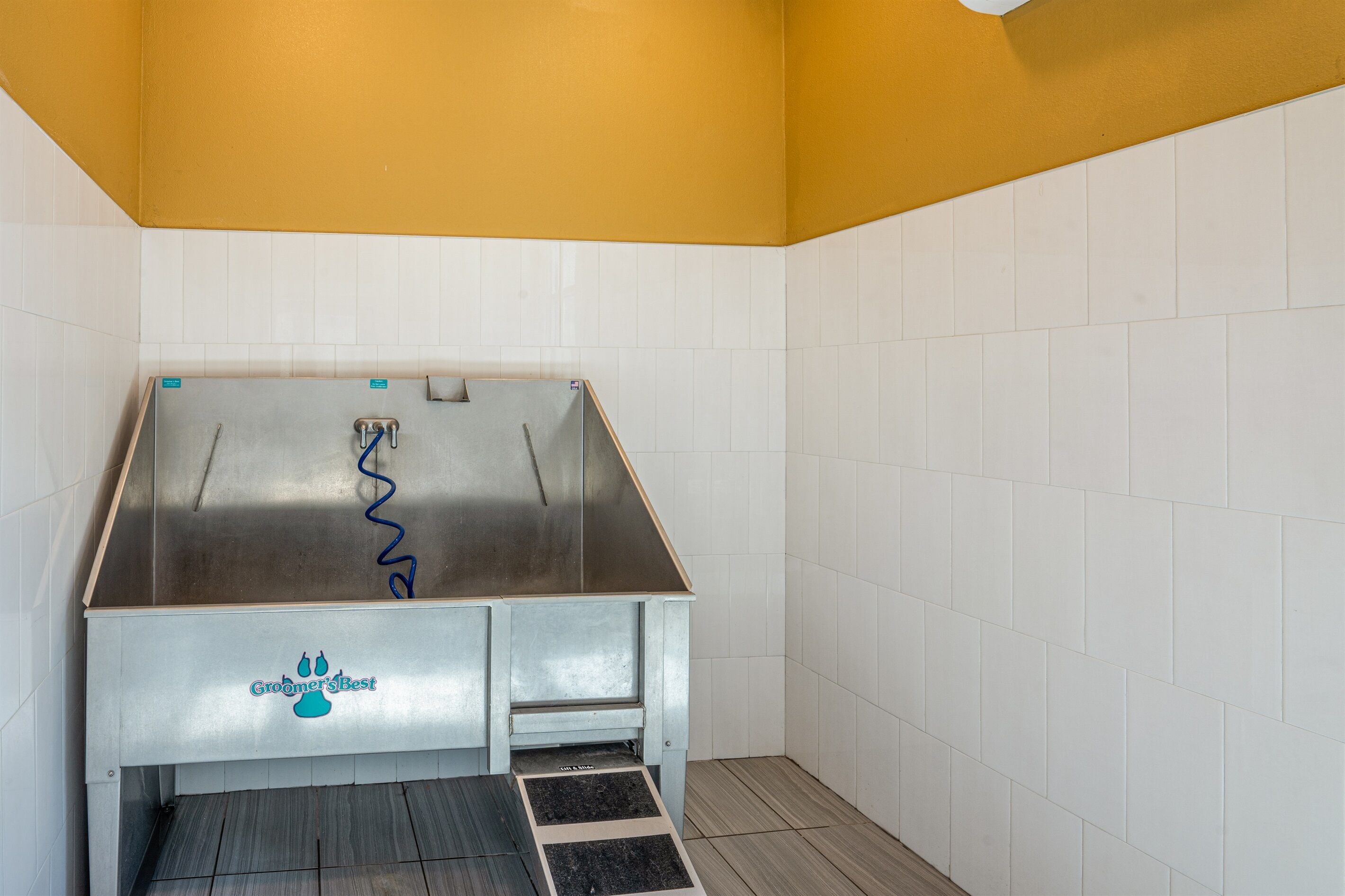 A bathroom with a stainless steel sink, white tiled walls, and a yellow ceiling.