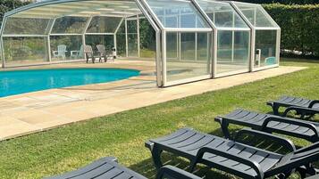 Un espace piscine entièrement vitré, avec des chaises longues et un ciel d’un bleu limpide.