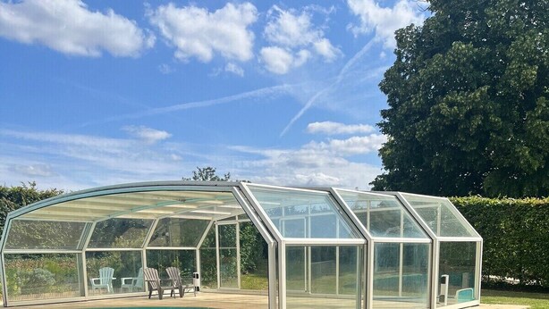 Ein von Glas umschlossener Poolbereich mit Liegestühlen und blauem Himmel.