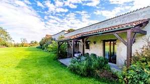 Ein Haus mit überdachter Terrasse, einem Rasen und einem Garten.