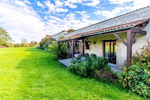 Ein Haus mit überdachter Terrasse, einem Rasen und einem Garten.