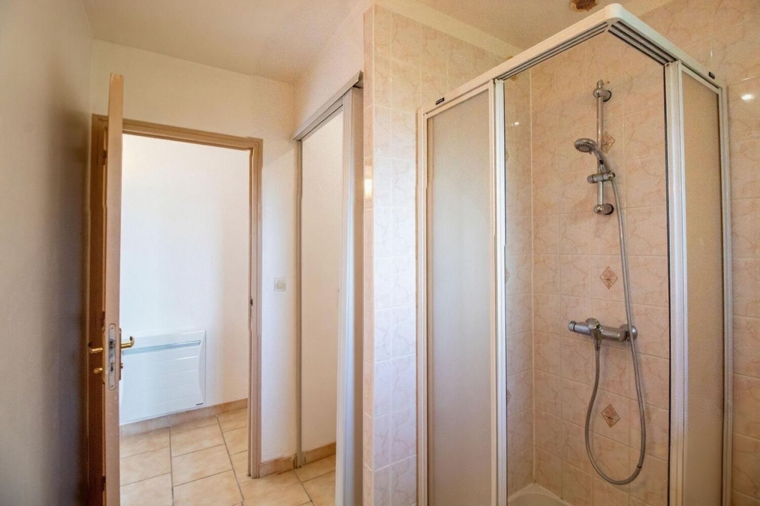 Et badeværelse med bruser, toilet og en dør til et andet rum.