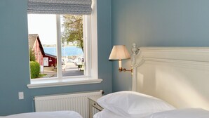 A bedroom with a bed, a window with a view of a dock and boats, and a wall-mounted lamp. - Hotel Baltic (Sydals)