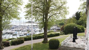 A view of a marina with boats docked, a lawn with a flagpole, and outdoor seating with umbrellas. - Hotel Baltic (Sydals)