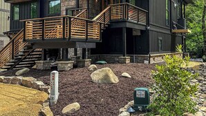 A modern two-story house with a stone foundation, wooden deck, and a stone retaining wall.