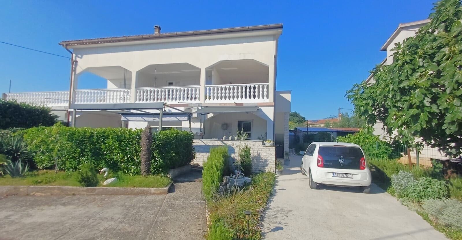 A two-story building with a balcony, a driveway, and a parked car.