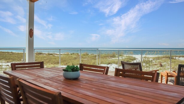 A wooden table with chairs and a potted plant, overlooking a beach with a clear sky. - Modern Coastal Design ~ Sea La Vie (Mexico Beach)