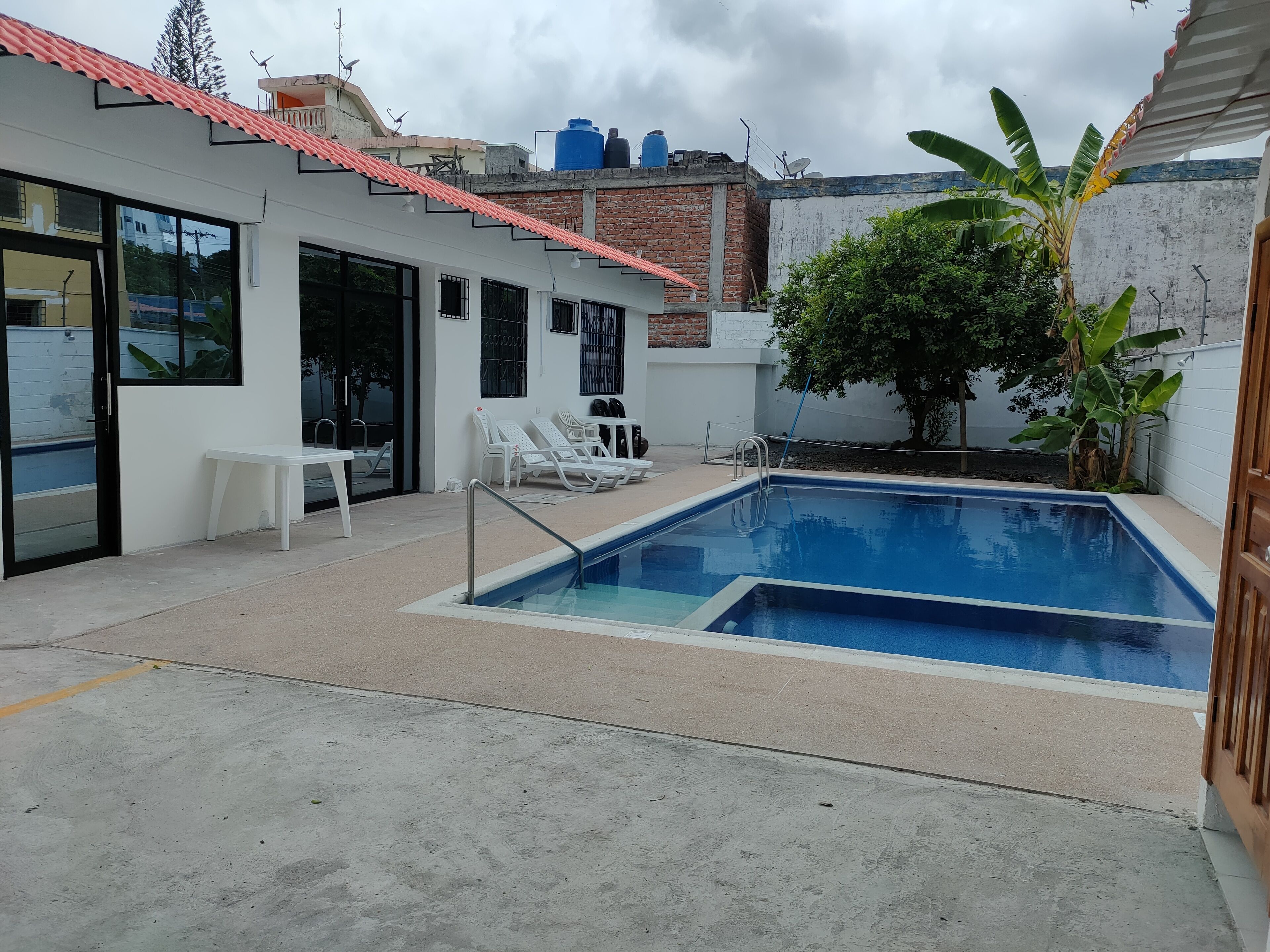 Una piscina con sillas de descanso, un banco y una planta en maceta.