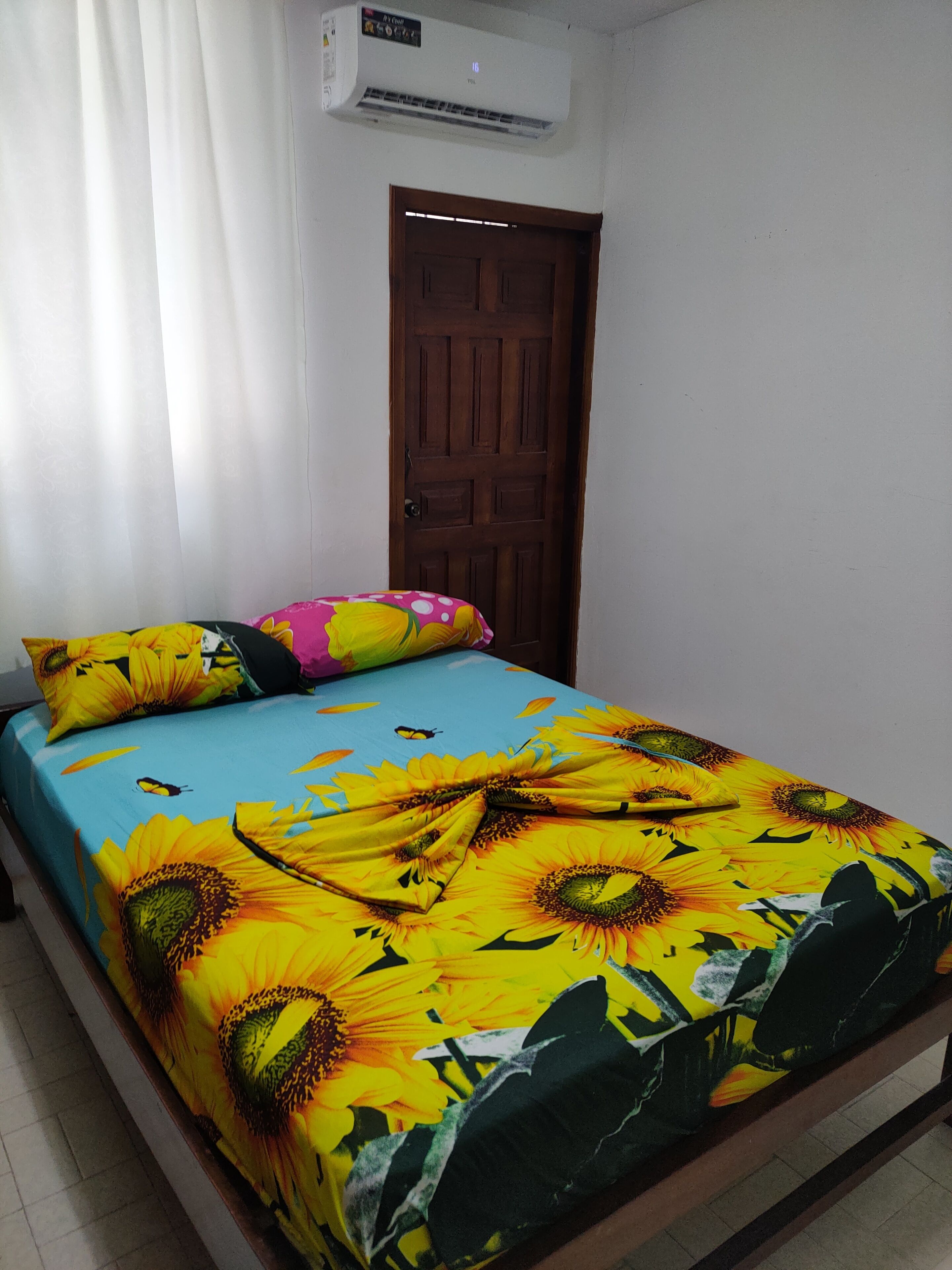 A bed with a sunflower and butterfly bedspread, a wooden door, and an air conditioning unit on the wall.