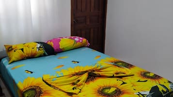 A bed with a sunflower and butterfly bedspread, a wooden door, and an air conditioning unit on the wall.