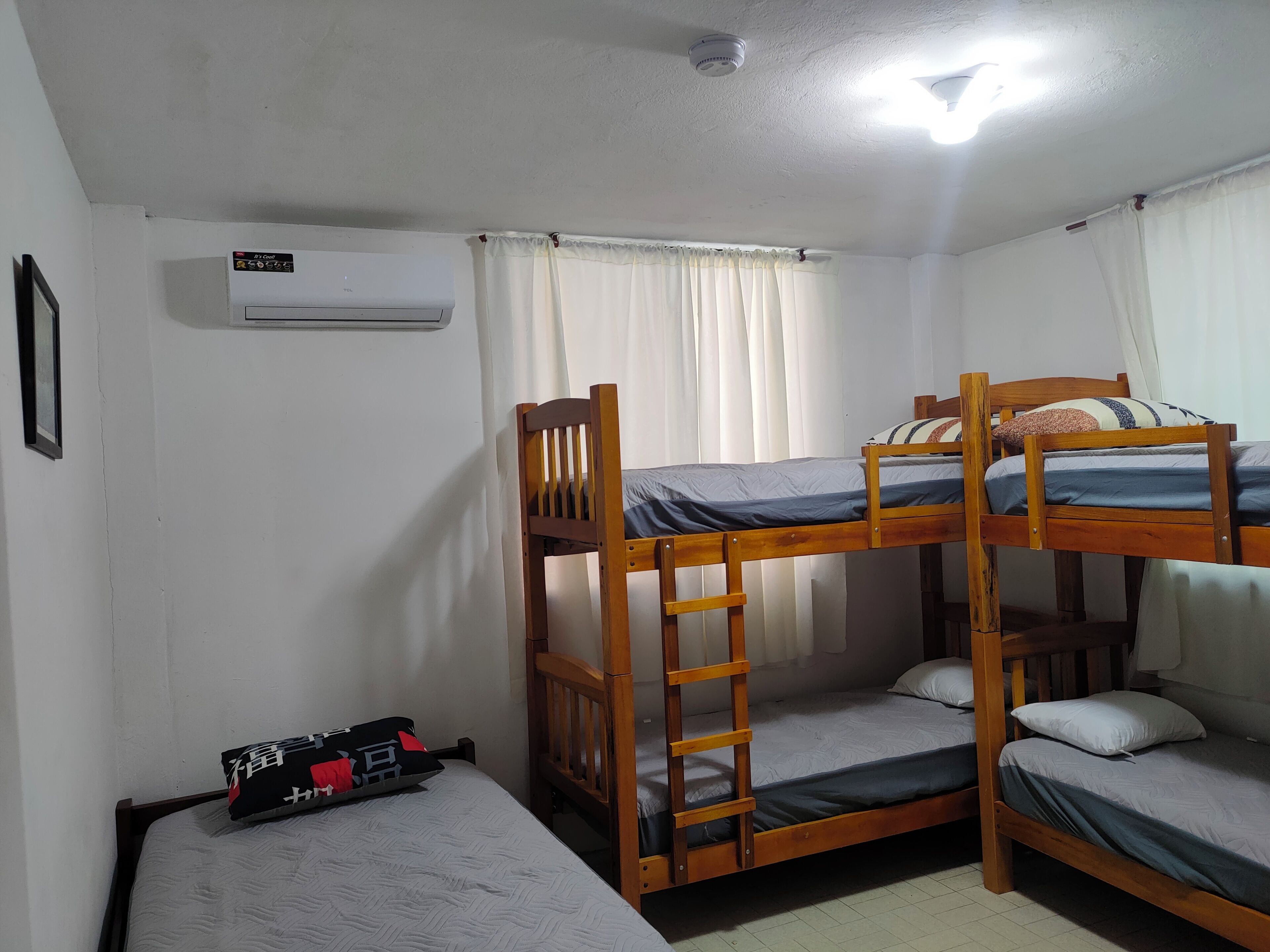 Una habitación tipo dormitorio con literas, una escalera, una mesita con una silla y un equipo de aire acondicionado.