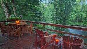 A wooden deck with a table and chairs, overlooking a river.