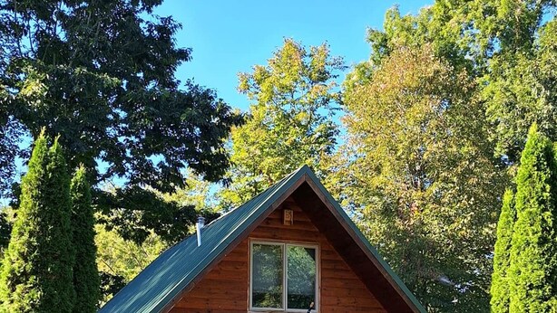 A wooden cabin with a pitched roof, a front porch, and an American flag.