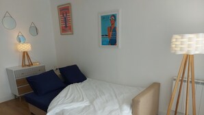 A bedroom with a bed, bedside table, lamp, posters, and a floor lamp.