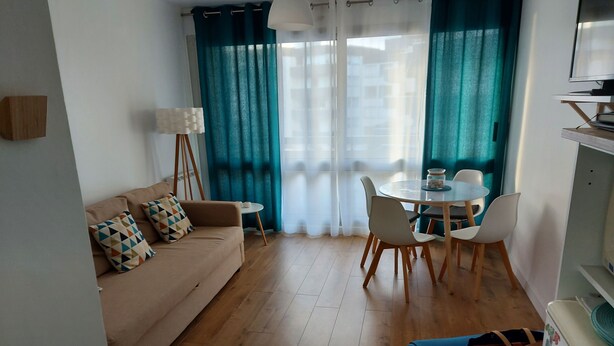 A living room with a sofa, a dining table with chairs, a lamp, and a TV.