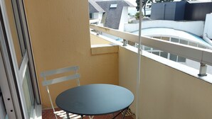 A small outdoor balcony with a table and chairs, a black umbrella, and a white railing.