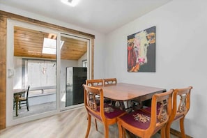 Ein Essbereich mit Holztisch und -stühlen, einer Glastür zum Außenbereich und einem Gemälde an der Wand.