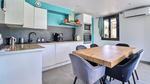 A modern kitchen with white cabinets, a wooden dining table, and black chairs. - Superbe Villa 6 Couchages + un lit Bébé, Jacuzzi, Piscine, Salle de Sport, Calme (Bouillargues)