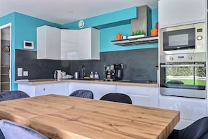 Een moderne keuken met witte kasten, een houten eettafel en een inbouwoven.