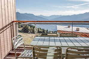 Ein Balkon mit Tisch und Stühlen, mit Blick auf eine gebirgige Landschaft.