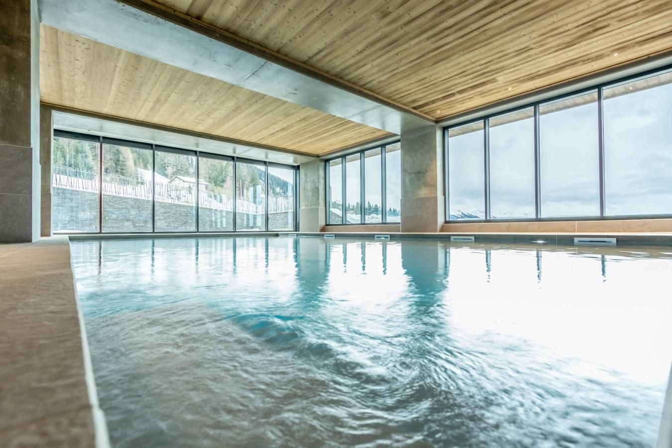 An indoor swimming pool with large windows and a wooden ceiling.