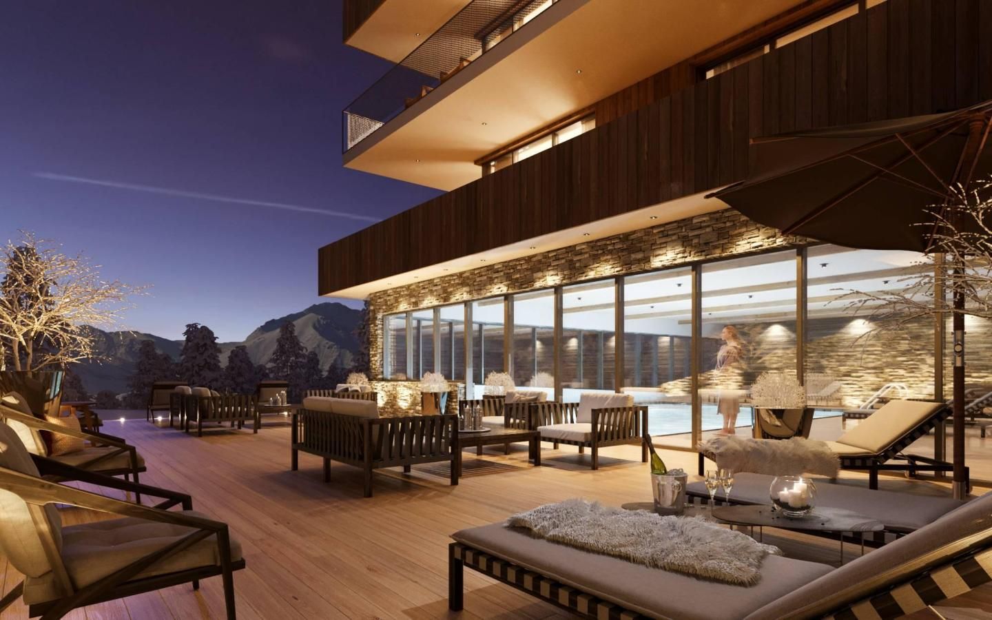 A modern outdoor lounge area with wooden flooring, multiple seating options including sofas and chairs, and a large glass wall offering a view of the mountains.
