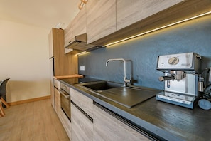 A modern kitchen with a stainless steel sink, a DeLonghi espresso machine, wooden cabinets, and a built-in oven. - 50m from ski slopes, fitness, swimming pool, sauna, hammam, terrace, ski locker, 75m², Les Arcs (Bourg-Saint-Maurice)