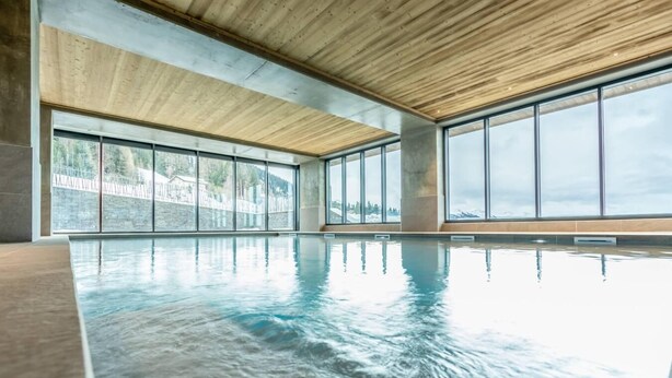 An indoor swimming pool with large windows and a wooden ceiling.