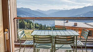 Un balcon avec une table et des chaises, donnant sur un paysage montagneux.