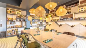 Un espace bar moderne avec une longue table en bois, des chaises à revêtement vert et des lampes suspendues. Des étagères sont remplies de différentes bouteilles.