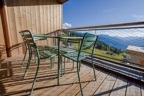 Une terrasse en bois avec une table et des chaises, offrant une vue sur un paysage montagneux.