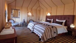 A tent-style room with a large bed, a chair, and a small table.