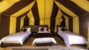 A tent-style room with three beds, each with white bedding and brown headboards.