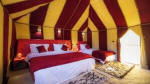 A tented accommodation with two beds, each with red bedding and white pillows, and a patterned rug on the floor.