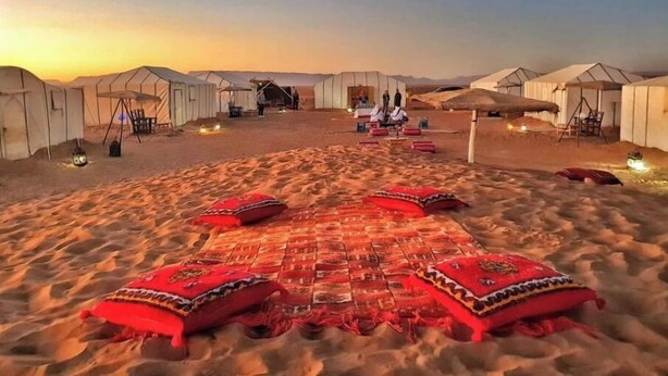A desert camp with tents and a central gathering area with a red carpet and cushions.