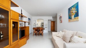 A spacious living room with a white sofa, wooden cabinets, and a dining area with chairs and a table.