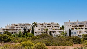 A multi-story residential building with balconies, surrounded by greenery and trees.