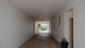 A narrow hallway with white walls and a tiled floor leading to a door at the end.