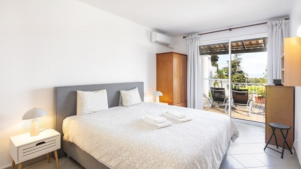 A bedroom with a bed, nightstand, lamp, wardrobe, and a view of the outdoors.