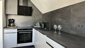 A modern kitchen with a built-in oven, a coffee maker, a kettle, and two wine glasses on the counter. - B&W Apartments - DG Wohnung (Morschen)