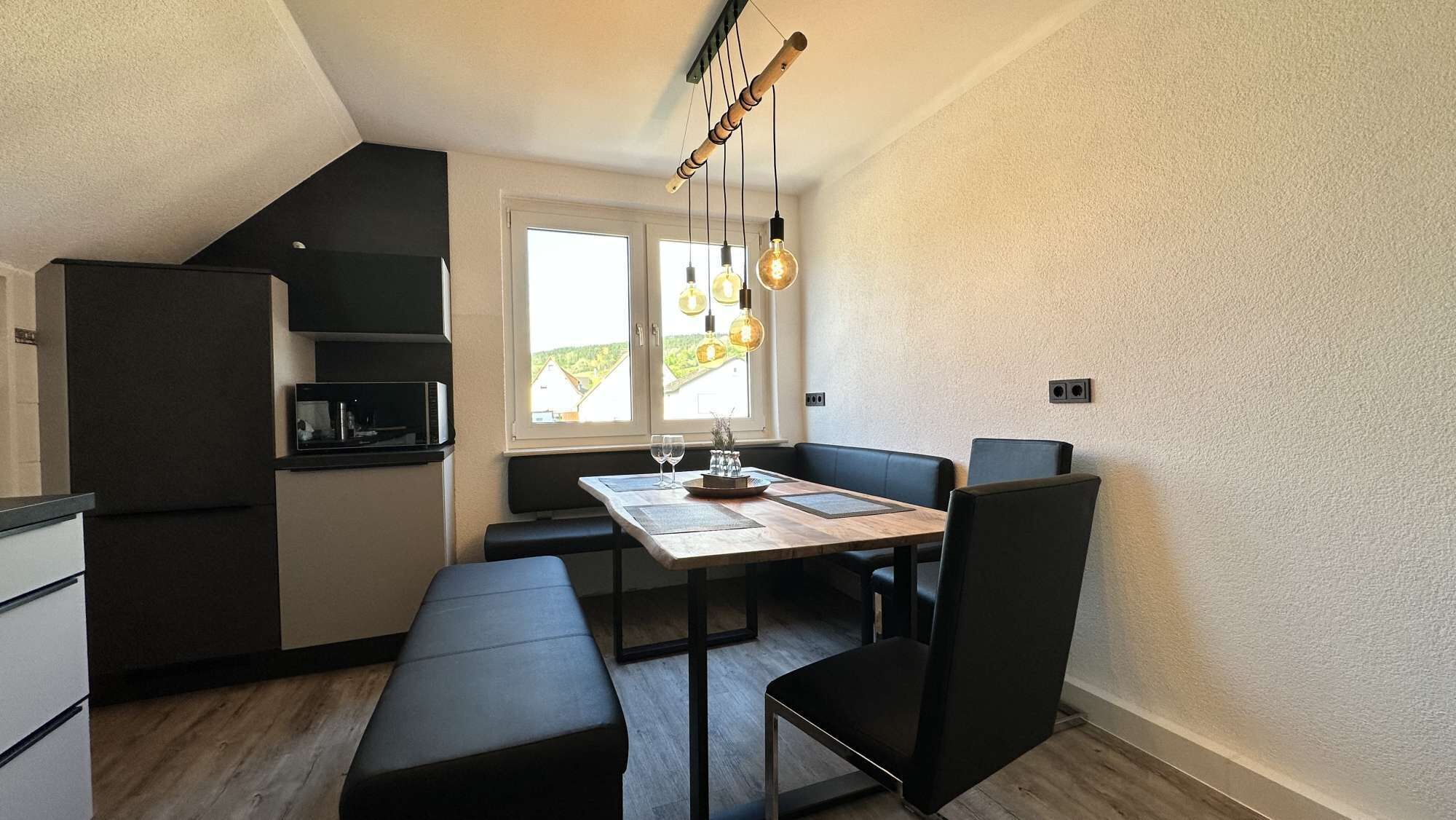 A compact kitchen with a built-in microwave, a black refrigerator, and a dining area with a wooden table and black chairs.