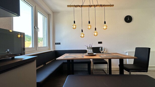 A modern kitchen with a wooden dining table, black chairs, and pendant lights. - B&W Apartments - DG Wohnung (Morschen)