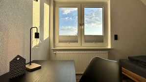 A room with a window, radiator, and a table with a lamp and a sign. - B&W Apartments - DG Wohnung (Morschen)