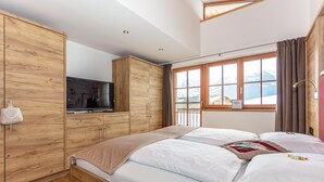 Een slaapkamer met een bed, een houten garderobe, een televisie en een raam met uitzicht op de bergen.