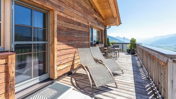 Een houten chalet met een balkon, grote ramen en uitzicht op bergen.