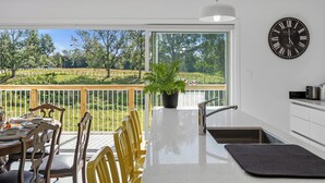 A modern kitchen with a large window, a dining area with yellow chairs, and a potted plant. - The Whitehouse - Lepperton Holiday Home (New Plymouth)