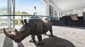 A modern living room with a glass coffee table, a black sofa, and a large rhinoceros sculpture. - The Whitehouse - Lepperton Holiday Home (New Plymouth)