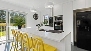 A modern kitchen with a large island, stainless steel appliances, and a view of the outdoors. - The Whitehouse - Lepperton Holiday Home (New Plymouth)