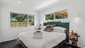 A bedroom with a large bed, two windows, a nightstand, and a statue. - The Whitehouse - Lepperton Holiday Home (New Plymouth)