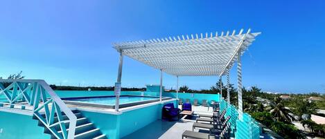 Ein Poolbereich auf dem Dach mit einer Pergola, Treppen, Liegestühlen und Blick auf die umliegende Landschaft.